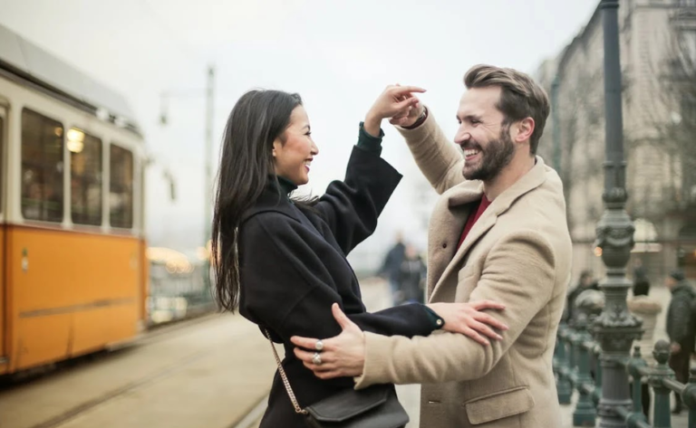 A man and woman dancing in a street smiling.