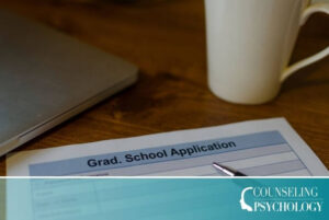A grad student's application materials sit on a desk, including a laptop, paper application, pen, and mug.