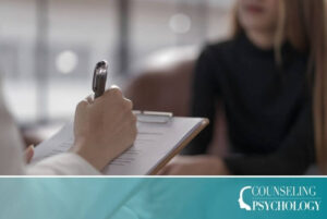 A close up of a mental health counselor's hand writing notes on a clipboard while meeting in an office with a patient.